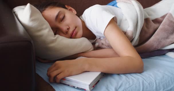 一个女孩抱着枕头下的一本书睡在4K的特写镜头中 她把毛毯拉直 舒服地躺在床上 — 图库视频影像