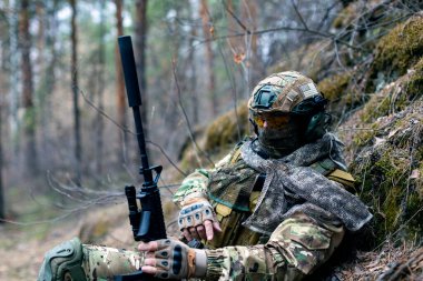 Modern savaş kavramı. Ormandaki çatışmadan sonra paralı asker dinleniyor. Çevreye uyum sağlayan kamuflajlı bir askerin yakın çekimi..