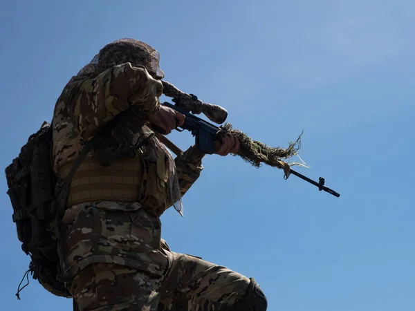 A professional special forces sniper aims at the enemy against the blue sky. Concept of modern military operations and a special operation on enemy territory.