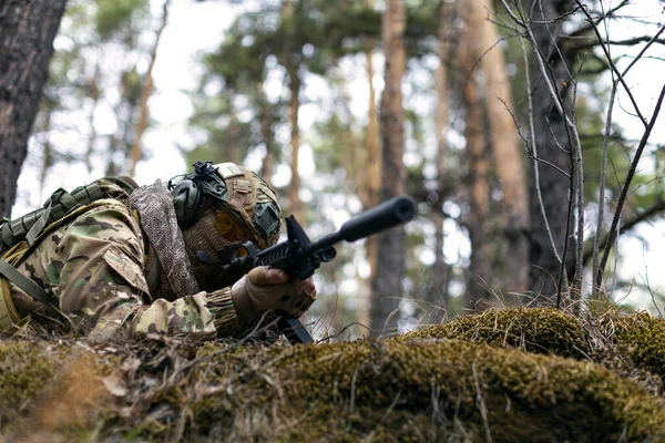 stock image Photo of a soldier aims at the enemy during a clash in the forest. The concept of modern warfare and special forces. Cropped image.