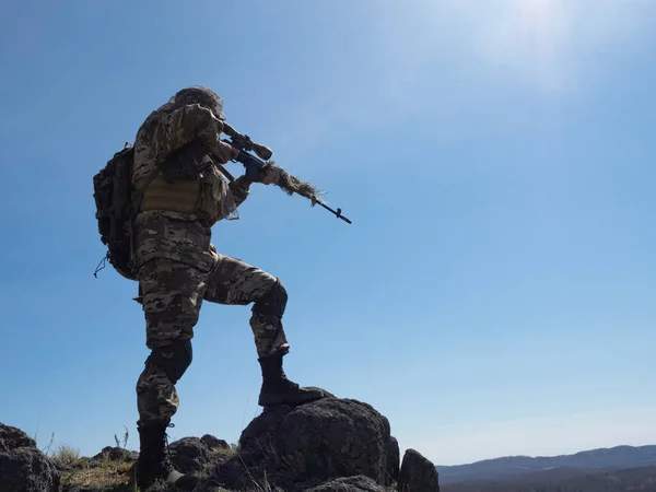 Professional special forces sniper during a special operation - he aims at the enemy. An ambush in mountains. Concept of modern military operations and a special operation on enemy territory.