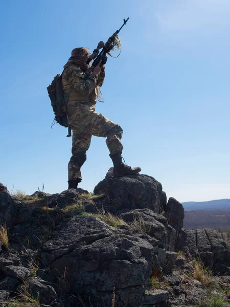 Professional special forces sniper during a special operation - he aims at the enemy. An ambush in mountains. Concept of modern military operations and a special operation on enemy territory. Vertical
