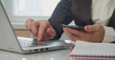 Ofiste akıllı telefonlu bir kadının elleri - bir kadın veriyi bilgisayara sokar, akıllı telefondaki bir mesajı kontrol eder.