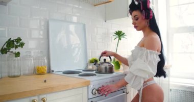 Güzel iç çamaşırlı genç seksi kadın sabahları mutfakta yemek pişiriyor. Çaydanlığı ocağa koyuyor. 4r görüntü.