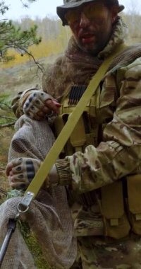 Yüzünde kan olan yaralı paralı asker kameraya bakıyor ve gözlüklerini çıkarıyor. Dikey 4k görüntü.