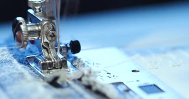 Dikiş makinesi iğnesinin hızlı hareketi. Dikiş makinesi mekanizmasının makro görüntüsü. Dikiş makinesine kot kumaşı dikiyorum. 4k 'lık yakın çekim..