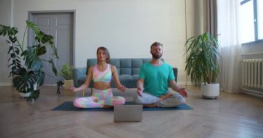 Orta yaşlı bir çift evde yoga dersi alarak meditasyon yapıyor. Yavaş çekim 4K görüntüsü.