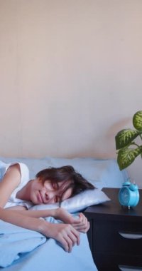 10 years old girl sleeps, wakes up, looks at the alarm clock and falls back to sleep. Vertical 4k footage 60fps.