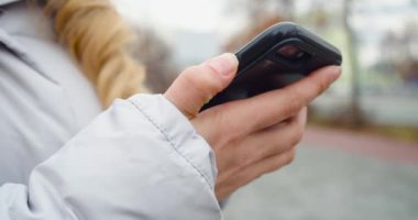 Close-up female hands with smartphone outdoor. A young woman turns on her smartphone and checks messages and news in social networks.