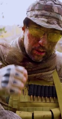 Close-up vertical video of a wounded soldier with a blood on the face looking at camera and take off his glasses. Vertical 4k footage.