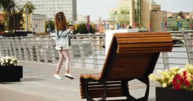 Urban coffee break - happy young woman dancing while walking along the embankment - she is listening to music on headphones using an online smartphone application. Slow motion 4k footage.