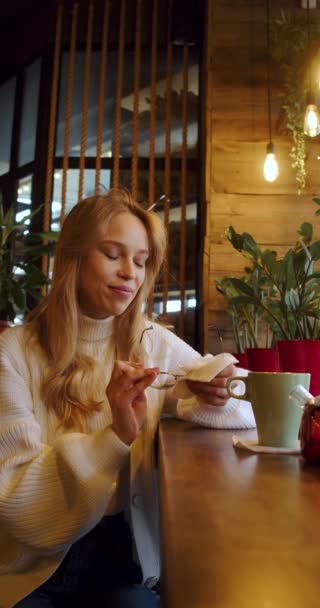 カフェに座っている間にメガネの表面を拭く若い女性 縦4K映像 スローモーション — ストック動画