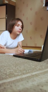 Vertical video of a schoolgirl doing homework online in front of a laptop monitor. Online education concept. Slow motion 4k footage.