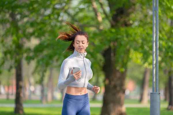 Young woman running in the city park in early morning. Attractive looking woman keeping fit and healthy. Sport and healthy lifestyle concept. Vertical photo.