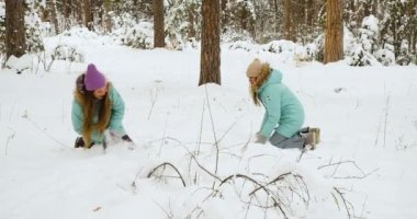 Two young women have fun in a snowy forest. They throw snow and have fun during the winter holidays. Slow motion 4k footage.