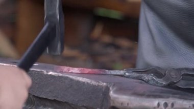 Hands and hammer of a blacksmith and his assistant forging a small piece of metal. Forge and Anvil. close-up 4k footage.