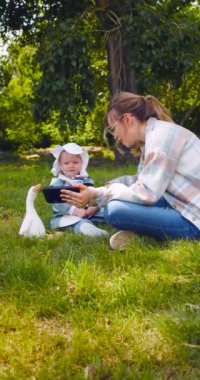 Young mother with a child watching interesting educational cartoon videos for children through an online application for a smartphone. Outdoor walking. Vertical 4k footage.