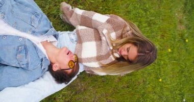 Two lesbians enjoy each other lying on the grass in the park. The concept of love and relationships. A beautiful romantic moment between two lovers. Vertical 4k footage.