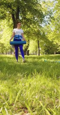 A woman is getting ready for an outdoor workout - she rolls out a mat and sits down to meditate and concentrate on the upcoming workout. Vertical 4k footage.
