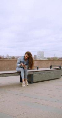 Great news - a woman with a smartphone in her hand is jumping with happiness. Urban scene outdoor. Slow motion vertical 4k footage.
