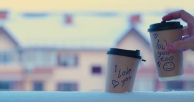 I love you and I love you too - male hand puts a glass of coffee in the snow with inscriptions. The concept of love and relationships. 4k slow motion. Video with copy space.