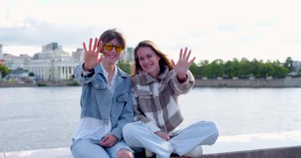 Lesbian Couple Sitting Embankment Waving Camera Making Heart Shape Fingers — Vídeo de Stock