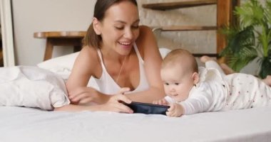 Young mother with newborn daughter watching cartoons through smartphone online application. Close-up 4k footage.