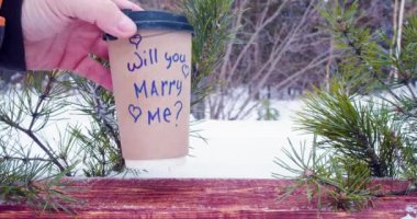 Will you marry me - yes, i will - male and female hands put paper cup with coffee in the snow with inscriptions. Love and relationships concept. Slow motion 4k footage.