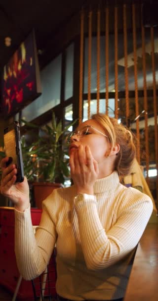カフェに座っている間 鏡としてスマートフォンを使っている美しい若い女性 スローモーション垂直4K映像 — ストック動画