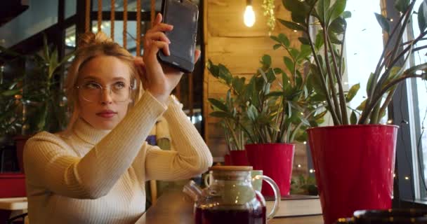 カフェに座っている間 鏡としてスマートフォンを使っている美しい若い女性 スローモーション4K映像 — ストック動画
