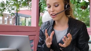 A young woman during online video call. She is sitting in a sidewalk cafe during an online video call in front of a laptop monitor. FHD footage.