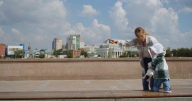 A young mother with her daughter are learning to walk on an outdoor walk. The first steps of a little girl. Slow motion outdoor footage.