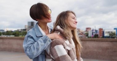 Two lesbian women sit on the embankment and enjoy each other. One woman massages her girlfriends neck ang embracing her. Beautiful romantic moment between two female lovers. 4k footage. Slow motion.