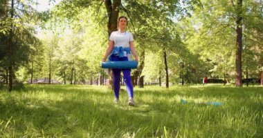 A woman is getting ready for an outdoor workout - she rolls out a mat and sits down to meditate and concentrate on the upcoming workout. 4k footage.