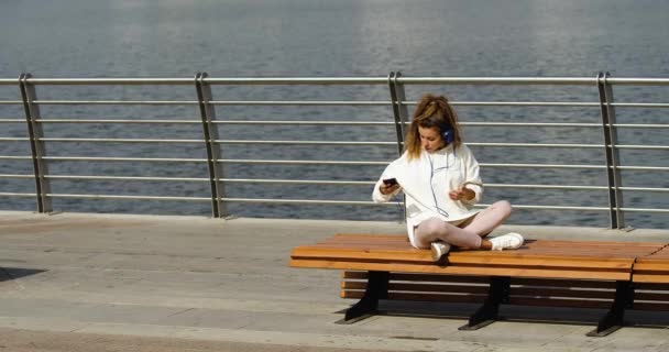 Young Woman Sits Bench Bay She Puts Her Smartphone Begins — Vídeo de Stock