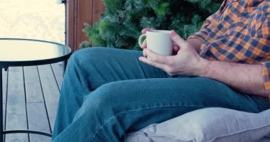 A man with a mug of coffee sits on a rocking chair on the terrace. The tranquility of an early morning in a country house. Slow motion 4k footage.