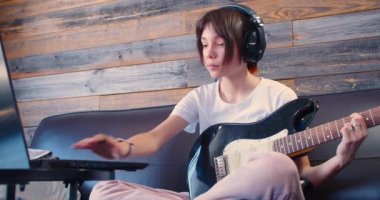 Slow motion 4k footage of a 10 years old girl with guitar in headphones in front of laptop monitor. She listening to the sound of her recorded guitar.