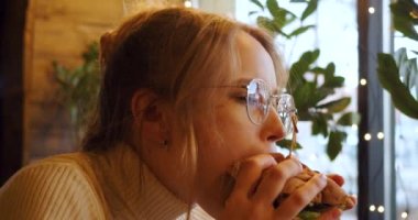 Footage of a young woman eating hamburger at a cafe. Slow motion 4k video. Close-up view.