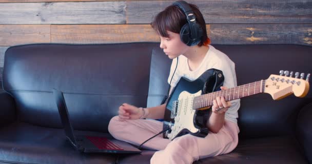 オンラインレッスン中の小さなギタリスト 10歳の少女がギターを持ってノートパソコンの前の家に座っている スローモーション4K映像 — ストック動画