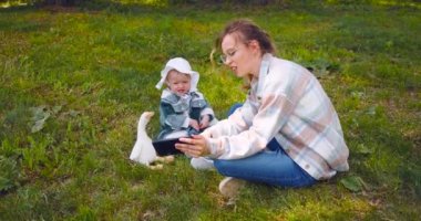 Young mother with a child watching interesting educational videos for children through an online application for a smartphone. Outdoor walking. 4k footage.