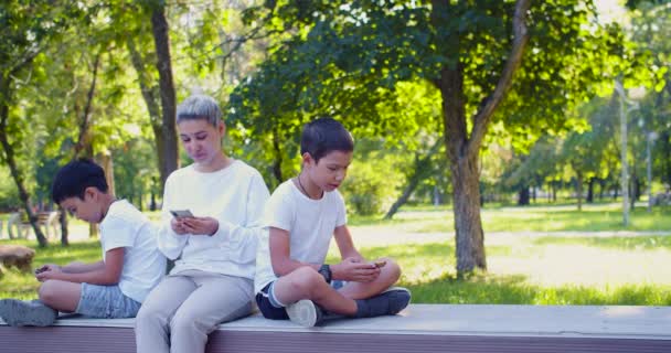 スマートフォン中毒 アジアの家族 母親と2人の息子は屋外のスマートフォンに埋葬された座っている 4K映像 — ストック動画