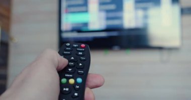 Close-up video of a male hand hand holding the TV remote control smart television. Internet online cinema - smart tv channel surfing. Slow motion 4k footage.