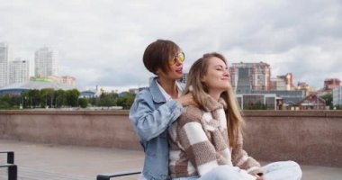 Two lesbian women sit on the embankment and enjoy each other. One woman massages her girlfriends neck. Beautiful romantic moment between two female lovers. 4k footage.