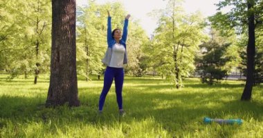Young woman during breathing exercises. She practices yoga in the park. 4k footage.