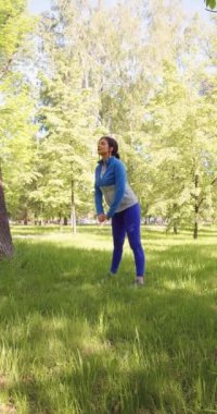 Vertical video of a 35-year-old woman practices yoga in a city park. She is doing a yoga flexibility exercise. 4k footage.