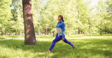 4k video of a 30-years-old woman practices yoga in a city park. She does a lunge exercise for balance.