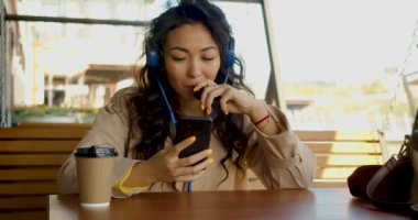 An Asian woman sits in headphones, messaging on social networks through an online smartphone app and smoking electronic cigarette. Modern addictions - smartphones and electronic cigarettes. 4k video