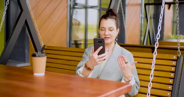 屋外カフェでのオンラインビデオ通話中に眼鏡の30歳の女性 4K映像 — ストック動画