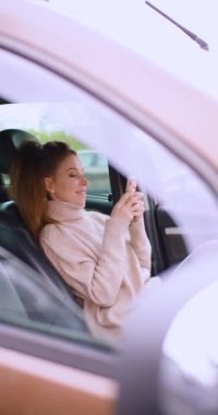 Online dating concept - a 30-year-old woman communicates with her boyfriend online messages via smartphone, in a car in a parking lot. She is in love. Vertical 4k footage.