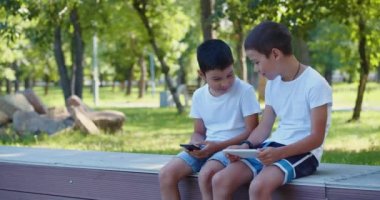 4k footage of a two boys are playing on their smartphones while walking outdoors - they are sitting on a bench, looking at their smartphones.